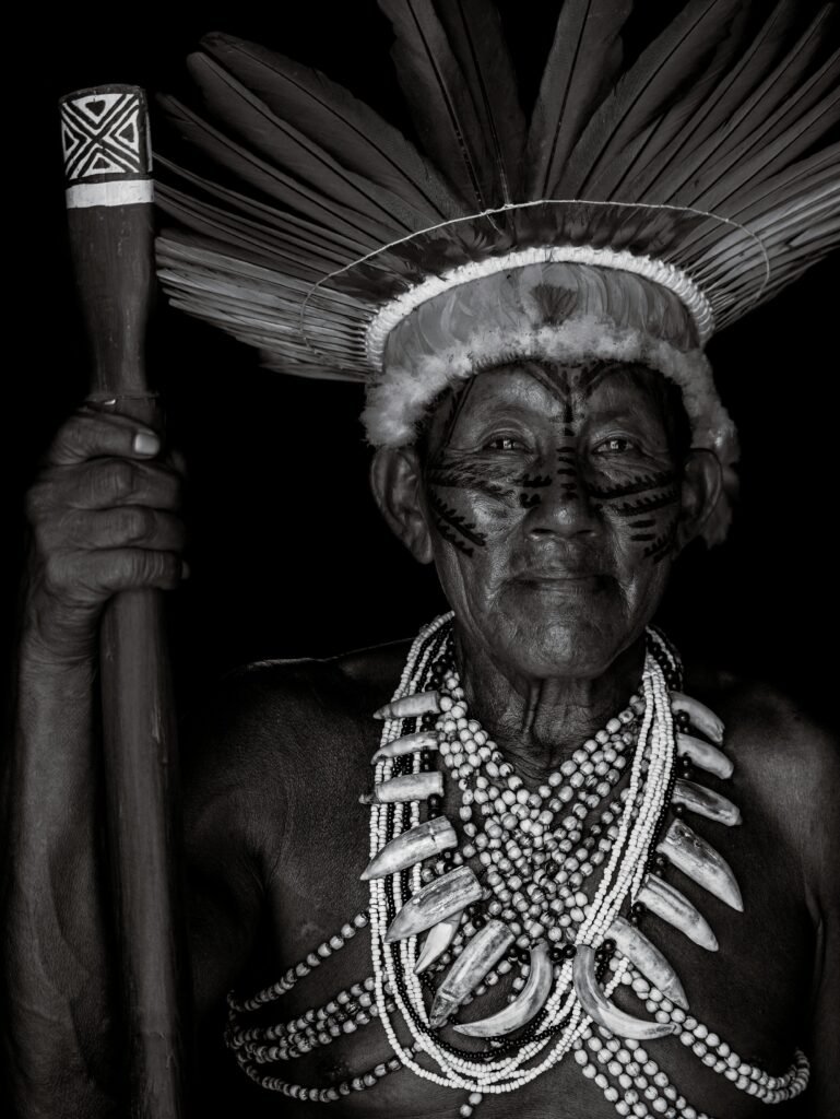 Black and white portrait of an indigenous elder wearing traditional headdress and necklaces in Manaus, Brazil.